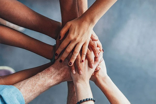 Multi-racial group of people putting their hands together.